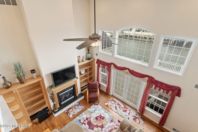 living room featuring ceiling fan, wood finished floors, a glass covered fireplace, and a towering ceiling