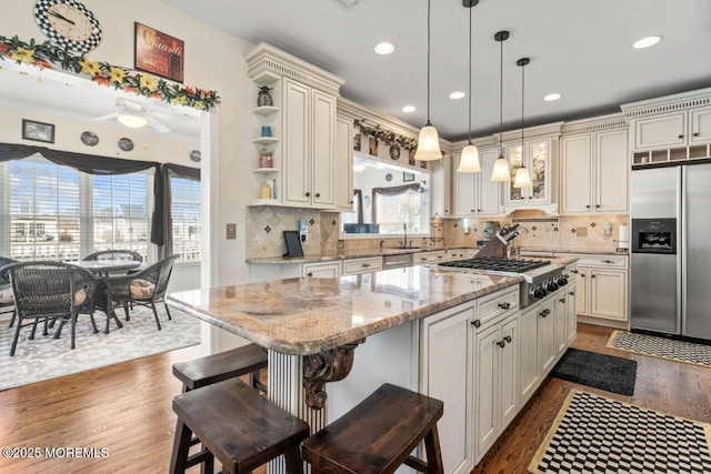 kitchen with light stone counters, stainless steel appliances, a breakfast bar, a center island, and open shelves