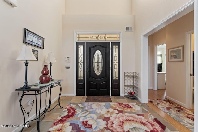 foyer entrance featuring a towering ceiling, baseboards, and visible vents