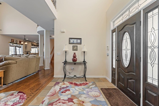 foyer entrance with light wood finished floors, decorative columns, baseboards, a high ceiling, and stairs