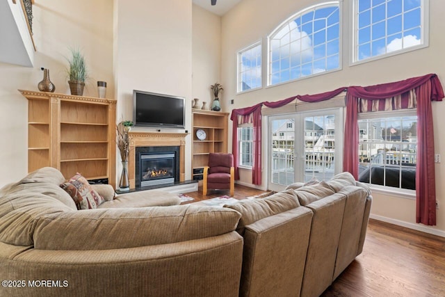 living room featuring a glass covered fireplace, wood finished floors, a high ceiling, and baseboards