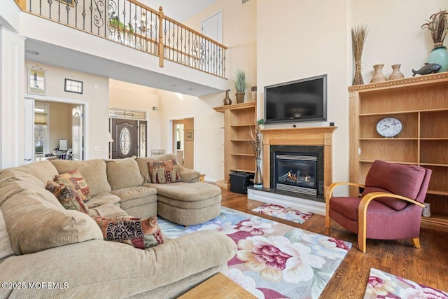 living room featuring a glass covered fireplace, a towering ceiling, and wood finished floors