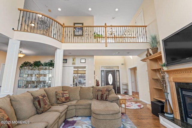 living room with a fireplace, decorative columns, a towering ceiling, and wood finished floors