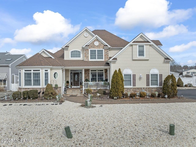 view of front of home with stone siding, a porch, and a shingled roof