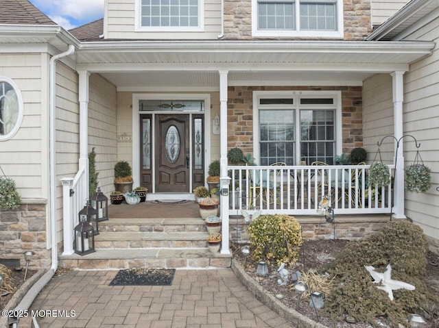 property entrance with stone siding, a shingled roof, and a porch