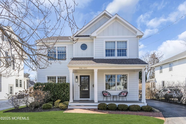 view of front facade featuring aphalt driveway, covered porch, fence, board and batten siding, and a front yard