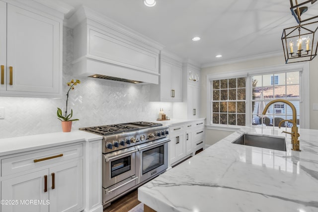 kitchen with range with two ovens, ornamental molding, white cabinets, a sink, and premium range hood