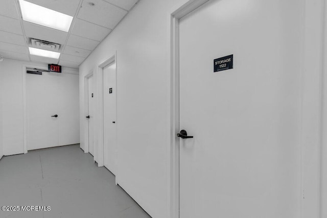 hallway with visible vents, a drop ceiling, and finished concrete flooring