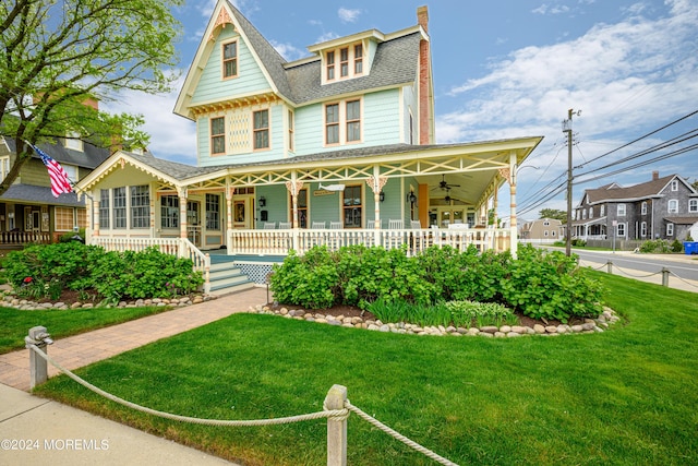 view of front of property with a ceiling fan, a chimney, roof with shingles, covered porch, and a front lawn