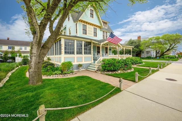 view of front of home featuring a front yard, a sunroom, and covered porch