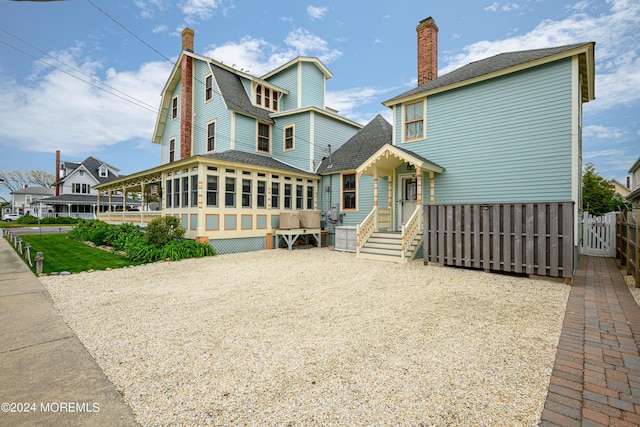 view of front of property with a chimney, a shingled roof, a gambrel roof, a sunroom, and fence