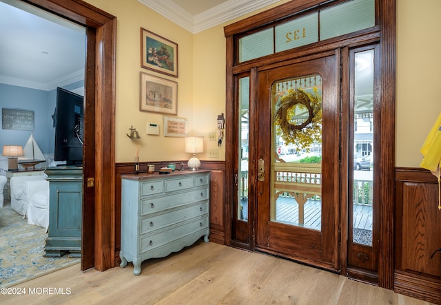 entrance foyer with ornamental molding, light wood-type flooring, and a wainscoted wall