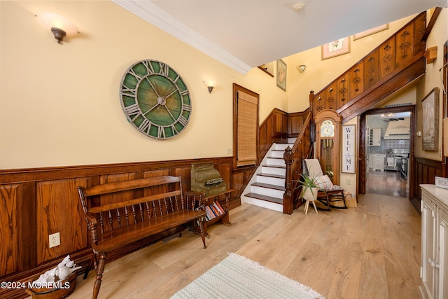 sitting room featuring light wood-type flooring, wainscoting, crown molding, and stairs