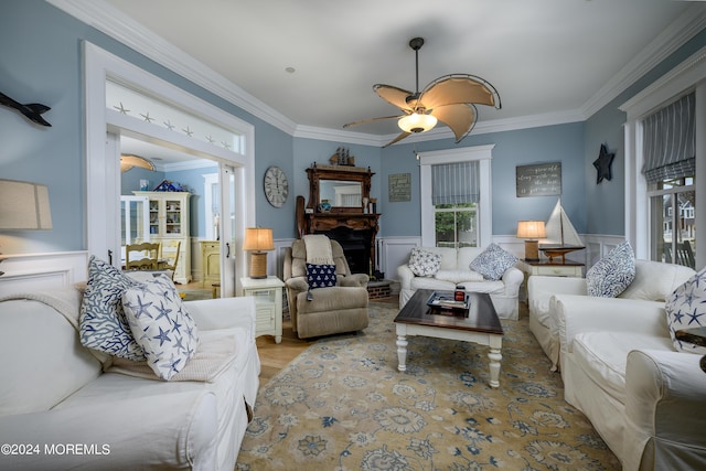 living area with a wainscoted wall, a fireplace with raised hearth, wood finished floors, and crown molding