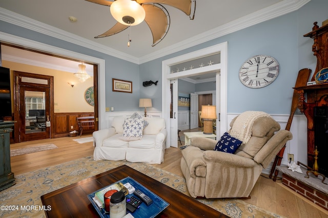 living area with a wainscoted wall, ceiling fan, light wood finished floors, and ornamental molding