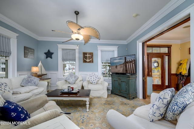 living area with a wainscoted wall, a ceiling fan, and crown molding