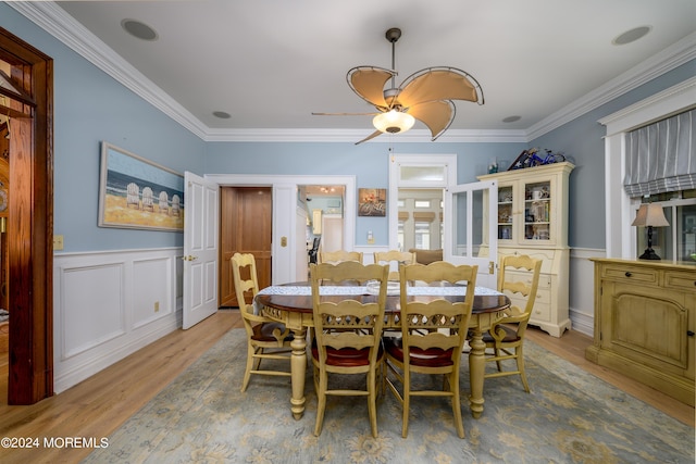 dining room featuring ornamental molding, a ceiling fan, a wainscoted wall, and wood finished floors