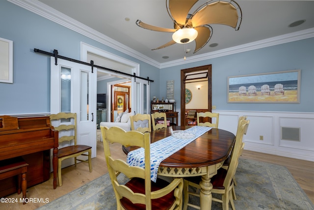 dining space featuring ornamental molding, ceiling fan, a barn door, and wood finished floors