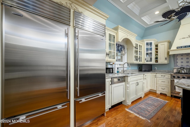 kitchen with stainless steel appliances, coffered ceiling, a sink, ornamental molding, and glass insert cabinets