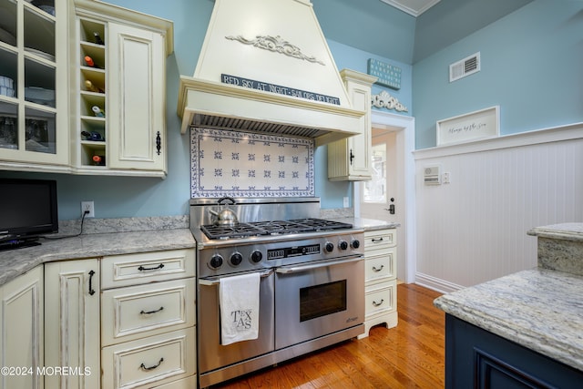 kitchen with light wood finished floors, visible vents, range with two ovens, glass insert cabinets, and cream cabinets