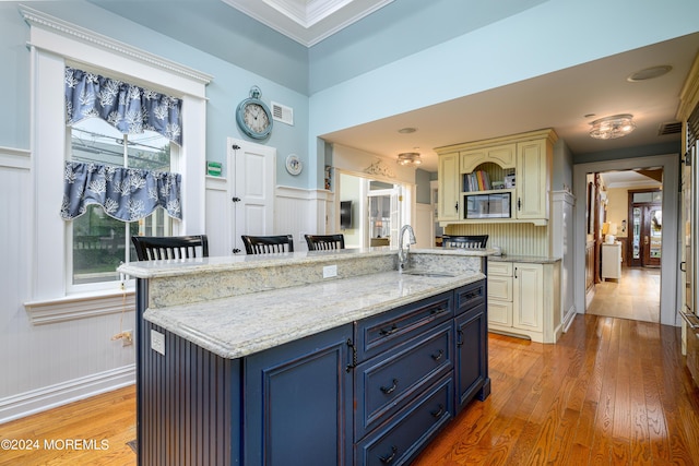 kitchen with blue cabinets, a sink, cream cabinetry, light wood finished floors, and stainless steel microwave