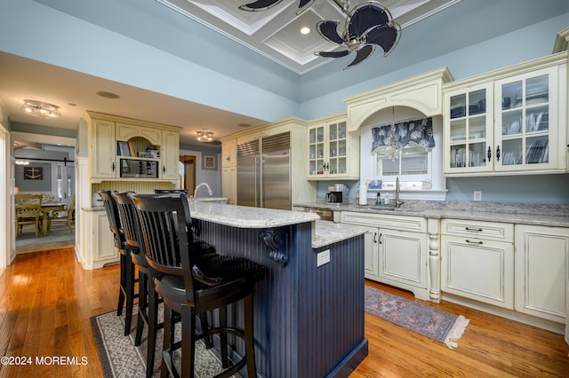 kitchen featuring built in appliances, coffered ceiling, a sink, a center island with sink, and glass insert cabinets