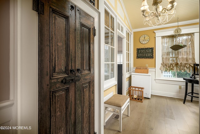 doorway featuring ornamental molding, light wood finished floors, wainscoting, and a chandelier