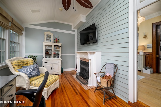 living area with crown molding, light wood-type flooring, a fireplace, and vaulted ceiling