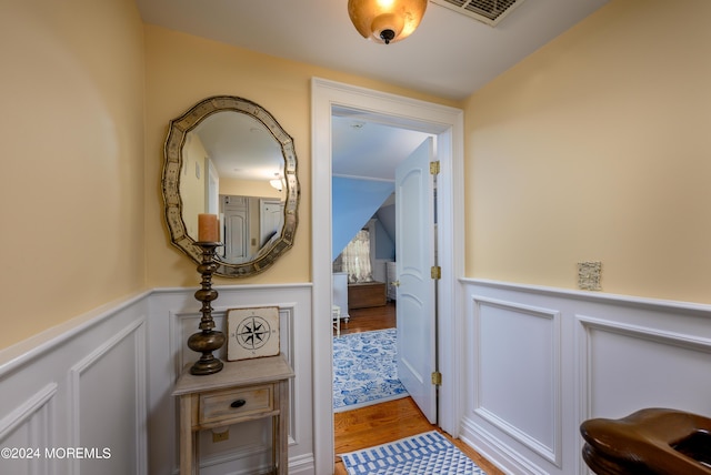 corridor with a wainscoted wall, visible vents, and wood finished floors