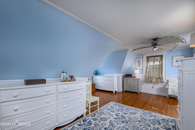 bedroom with a wainscoted wall, vaulted ceiling, dark wood finished floors, and a ceiling fan