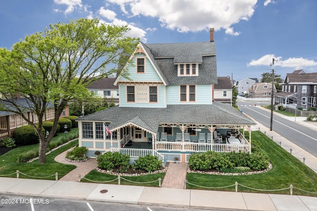 view of front facade featuring a sunroom, a shingled roof, a front yard, and a residential view