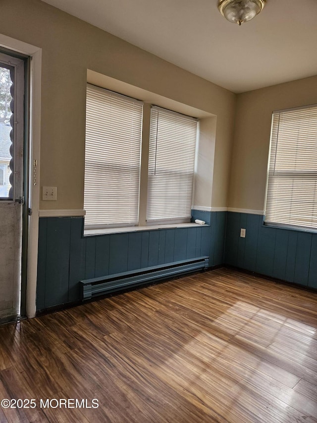 empty room with a wainscoted wall, baseboard heating, and wood finished floors