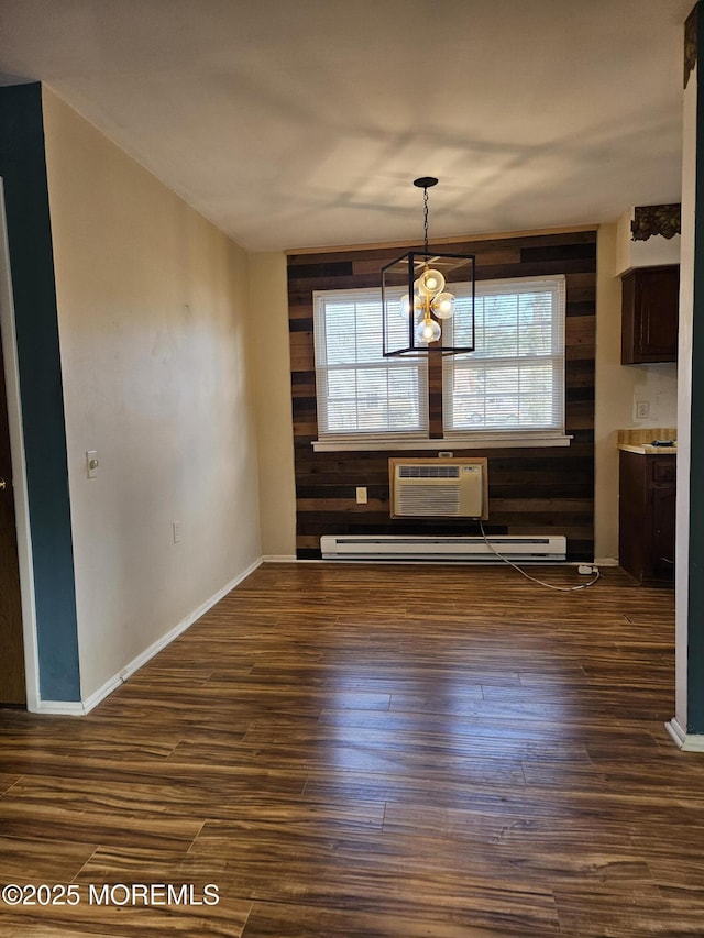 unfurnished dining area with dark wood-style floors, a notable chandelier, wood walls, a wall mounted air conditioner, and baseboards