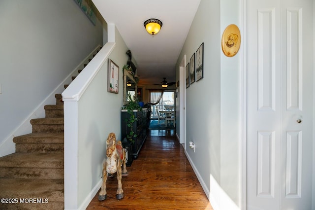 hallway featuring dark wood-type flooring, baseboards, and stairs