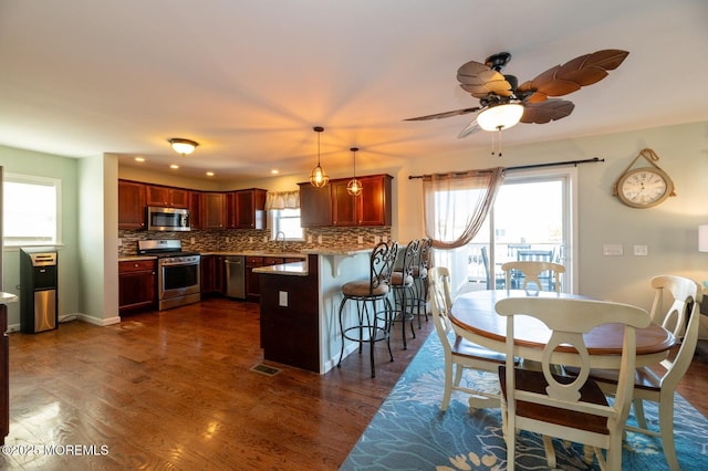 kitchen featuring pendant lighting, a breakfast bar area, light countertops, appliances with stainless steel finishes, and dark wood-type flooring