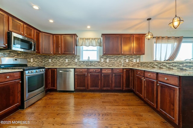 kitchen featuring a sink, hanging light fixtures, appliances with stainless steel finishes, light stone countertops, and dark wood-style floors