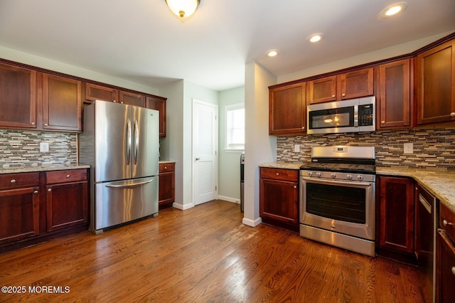 kitchen featuring appliances with stainless steel finishes, dark wood-type flooring, decorative backsplash, and light stone countertops