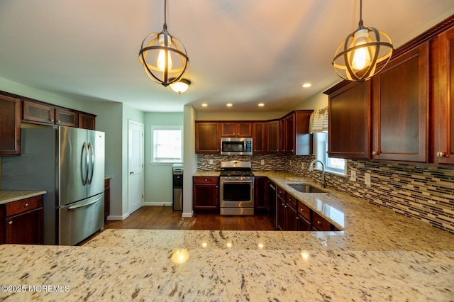 kitchen with stainless steel appliances, light stone counters, a sink, and pendant lighting