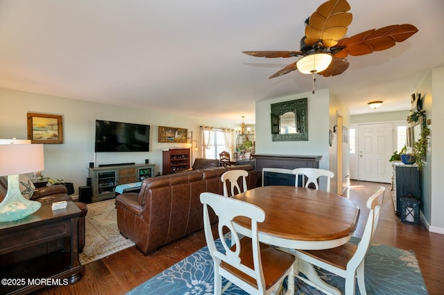 dining space featuring ceiling fan with notable chandelier, dark wood finished floors, and baseboards