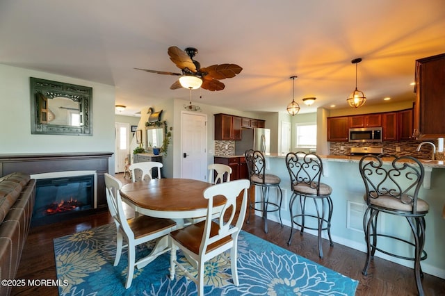 dining space featuring dark wood-style flooring, a glass covered fireplace, and a ceiling fan