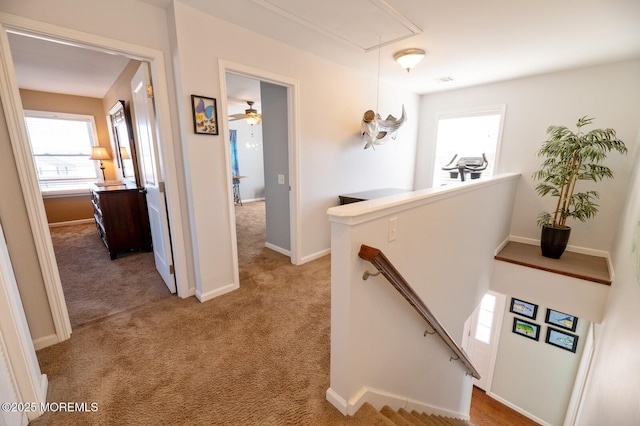 hall featuring attic access, baseboards, light colored carpet, and an upstairs landing