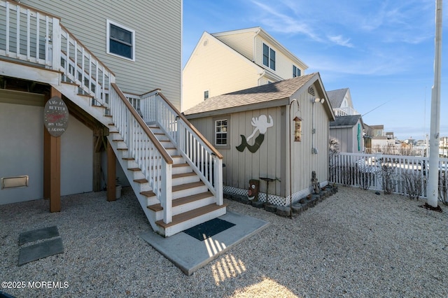 exterior space featuring a shingled roof, fence, and stairs