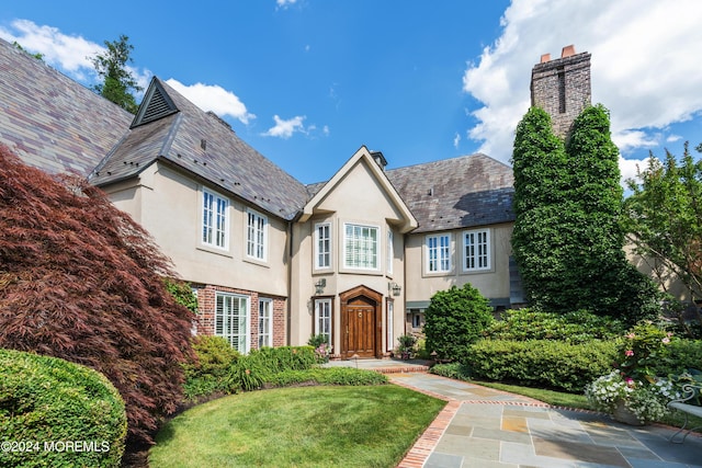 tudor house with brick siding, stucco siding, a front lawn, a chimney, and a high end roof