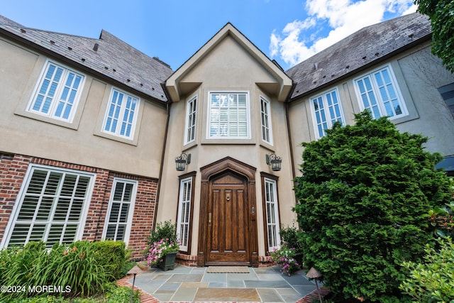 entrance to property with a high end roof, brick siding, and stucco siding