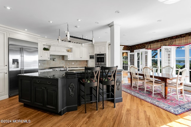 kitchen featuring a kitchen island with sink, white cabinetry, stainless steel appliances, and dark cabinetry