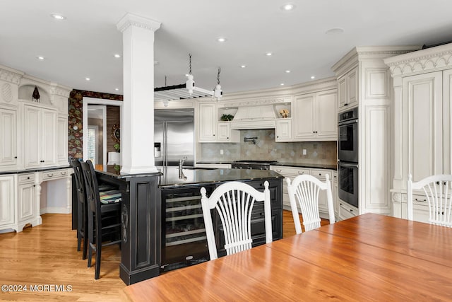 kitchen featuring beverage cooler, stainless steel appliances, white cabinetry, dark countertops, and a center island with sink