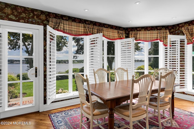 dining area with a water view, wallpapered walls, and wood finished floors