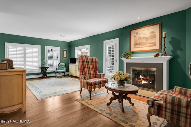 living area with recessed lighting, visible vents, baseboard heating, light wood-style floors, and a glass covered fireplace