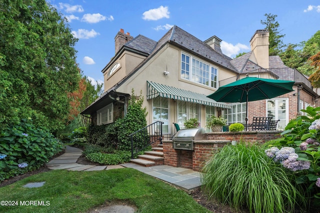 rear view of house with a chimney, a high end roof, area for grilling, and stucco siding