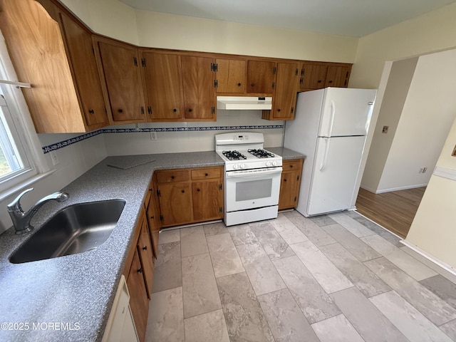 kitchen with a sink, brown cabinetry, white appliances, baseboards, and under cabinet range hood